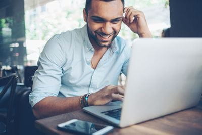 Un empleado sentado en una mesa, sonriendo mientras utiliza un ordenador, transmitiendo una actitud positiva en un entorno de trabajo.
